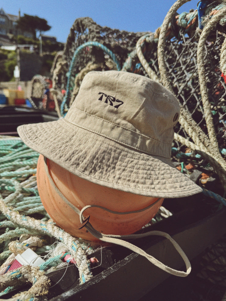 Beige bucket hat with logo on a pumpkin surrounded by fishing nets and equipment.