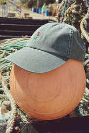 Green cap with floral embroidery on a wooden buoy surrounded by fishing nets.